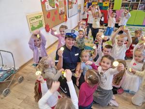 zdjęcie kolorowe w przedszkolu, policjantka kuca przy dzieciach
