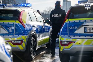 Dwa oznakowane radiowozy policyjne pomiędzy którymi stoi policjant