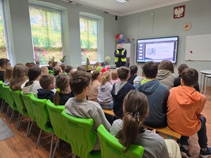 zdjęcie kolorowe, policjant stoi przed zebranymi dziećmi i przeprowadza prelekcję.