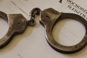 Zdjęcie przedstawia kajdanki leżące na teczce dochodzenia