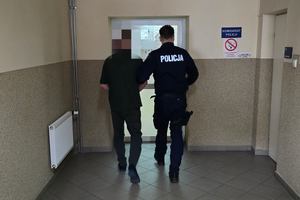 Zdjęcie przedstawia policjanta prowadzącego zatrzymanego mężczyznę