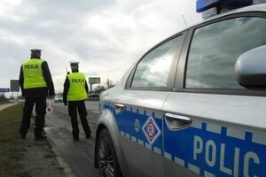 Zdjęcie przedstawia policjantów ruchu drogowego w odblaskowych kamizelkach stojących przed oznakowanym radiowozem