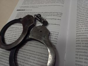 Zdjęcie przedstawia kajdanki policyjne leżące na otwartej książce