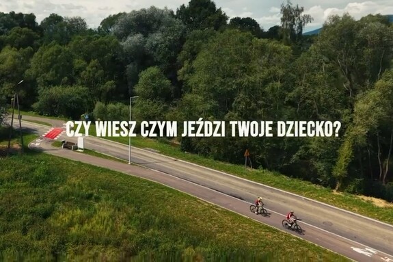 Rowery jadące ścieżka rowerową widziane z nagrania z lotu ptaka. Na środku napis: Czy wiesz czym jeździ Twoje dziecko?